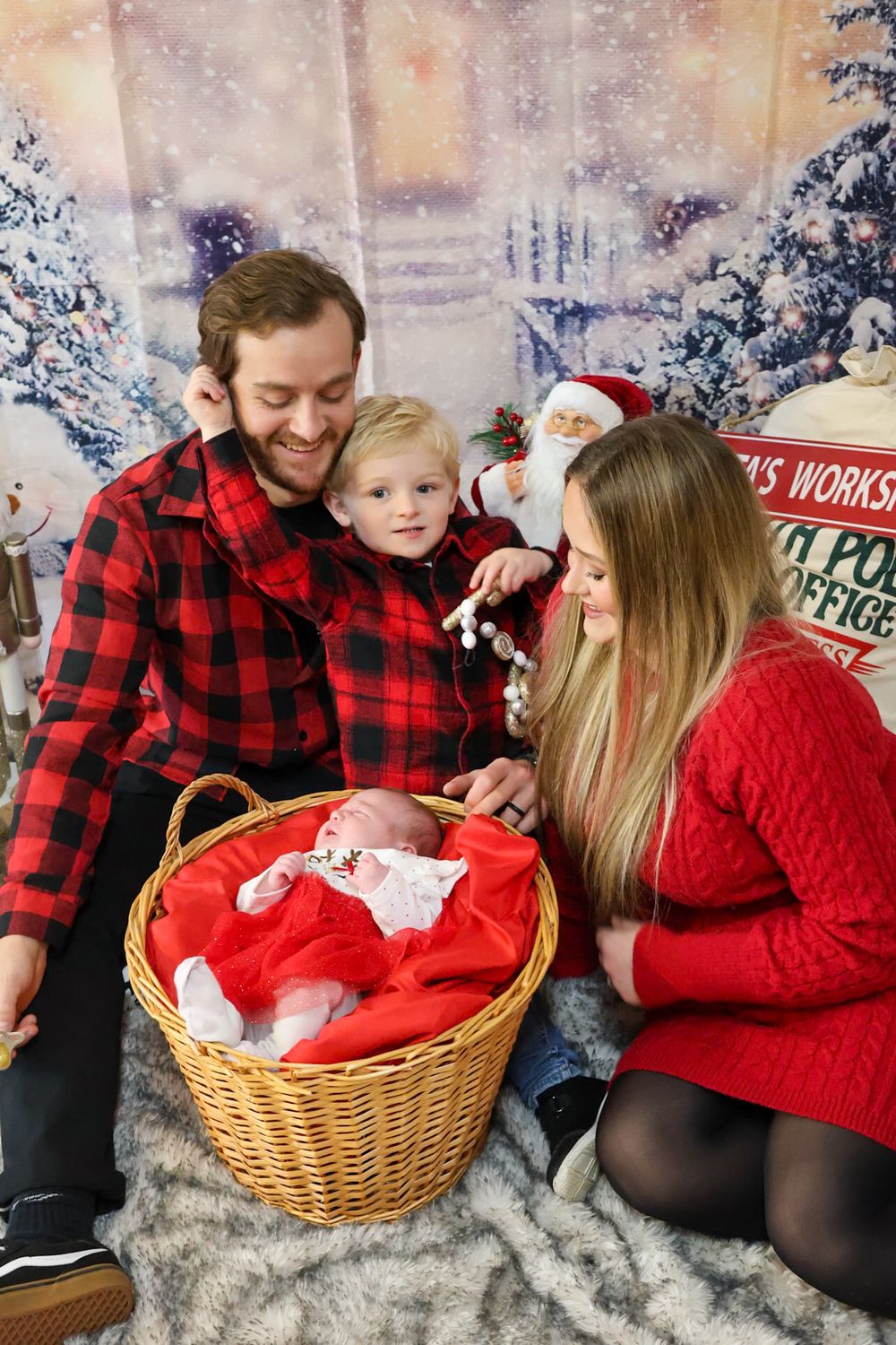 Family wearing red and black buffalo plaid sits together on cozy fur blanket during winter holiday photoshoot.