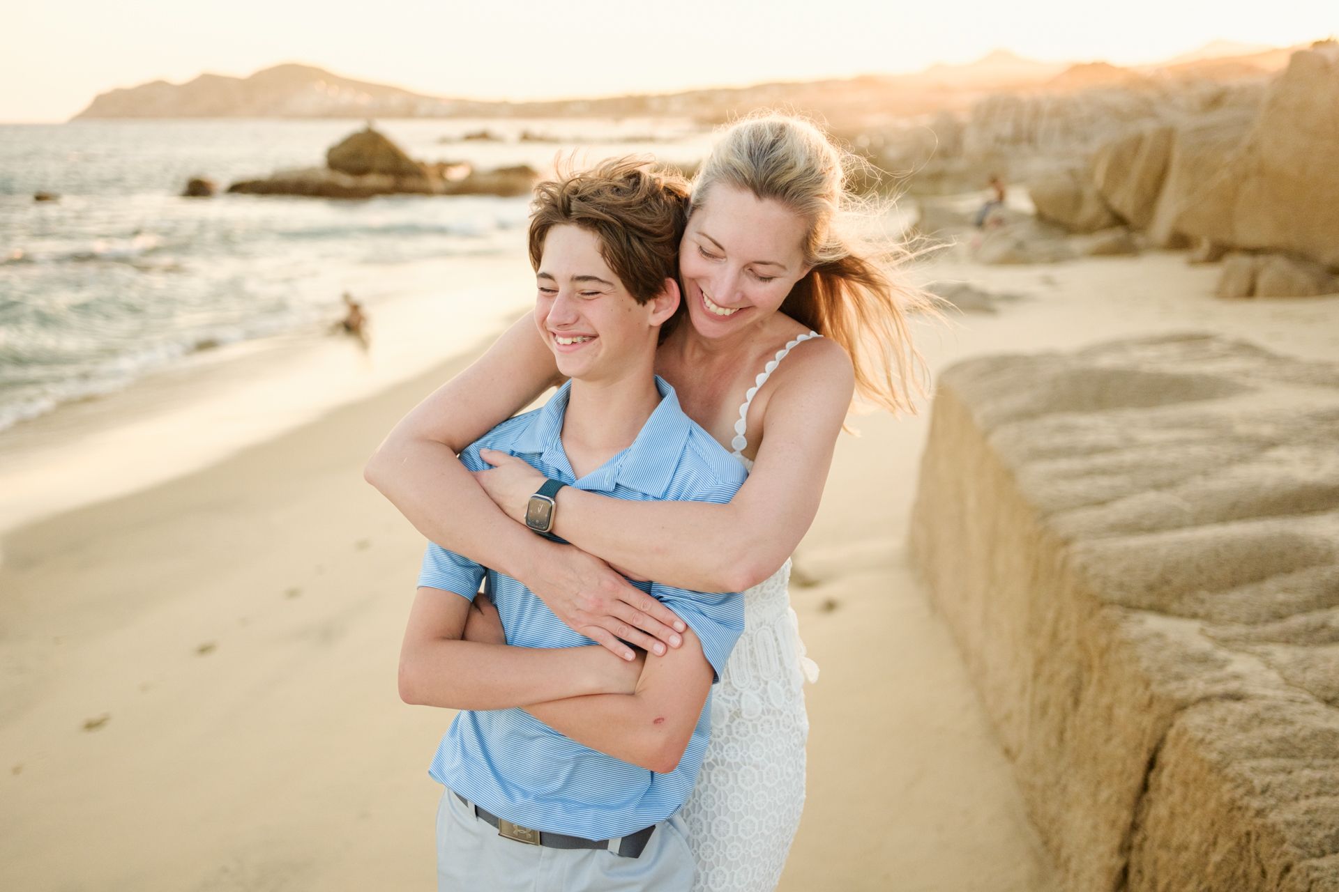 A family frolics and plays together on a sunny beach with white sand and blue ocean waves.