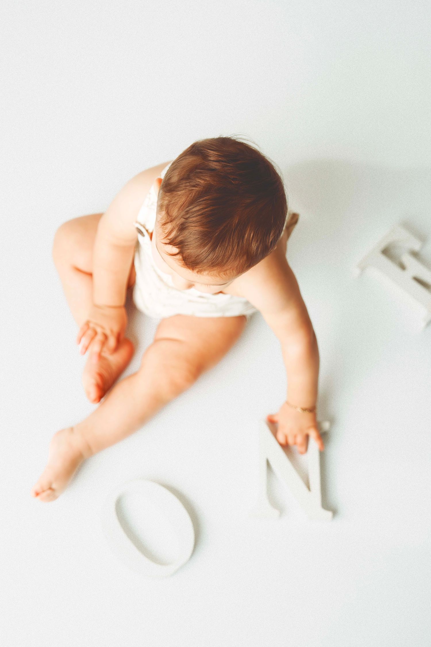 Overhead view of a baby in white sitting with number decorations on a light background.