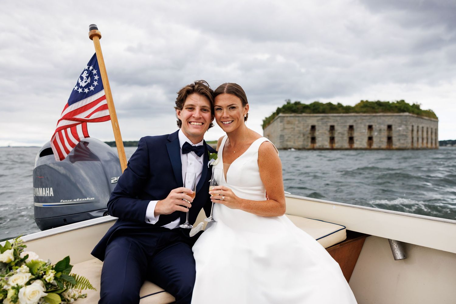 Wedding couple on boat with American flags and harbor views in background.