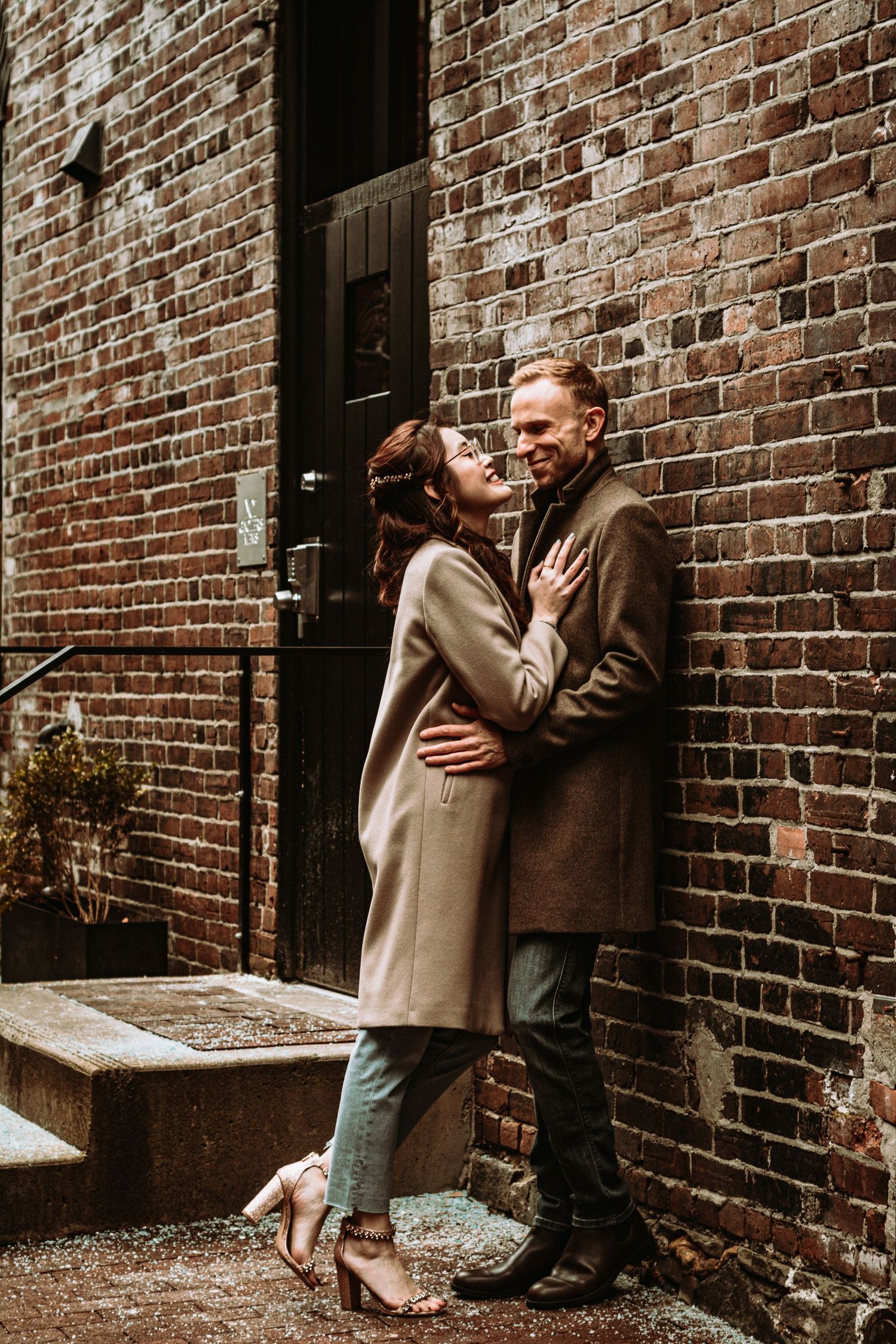 A romantic couple embraces against a rustic brick wall background in vintage-style engagement photography.