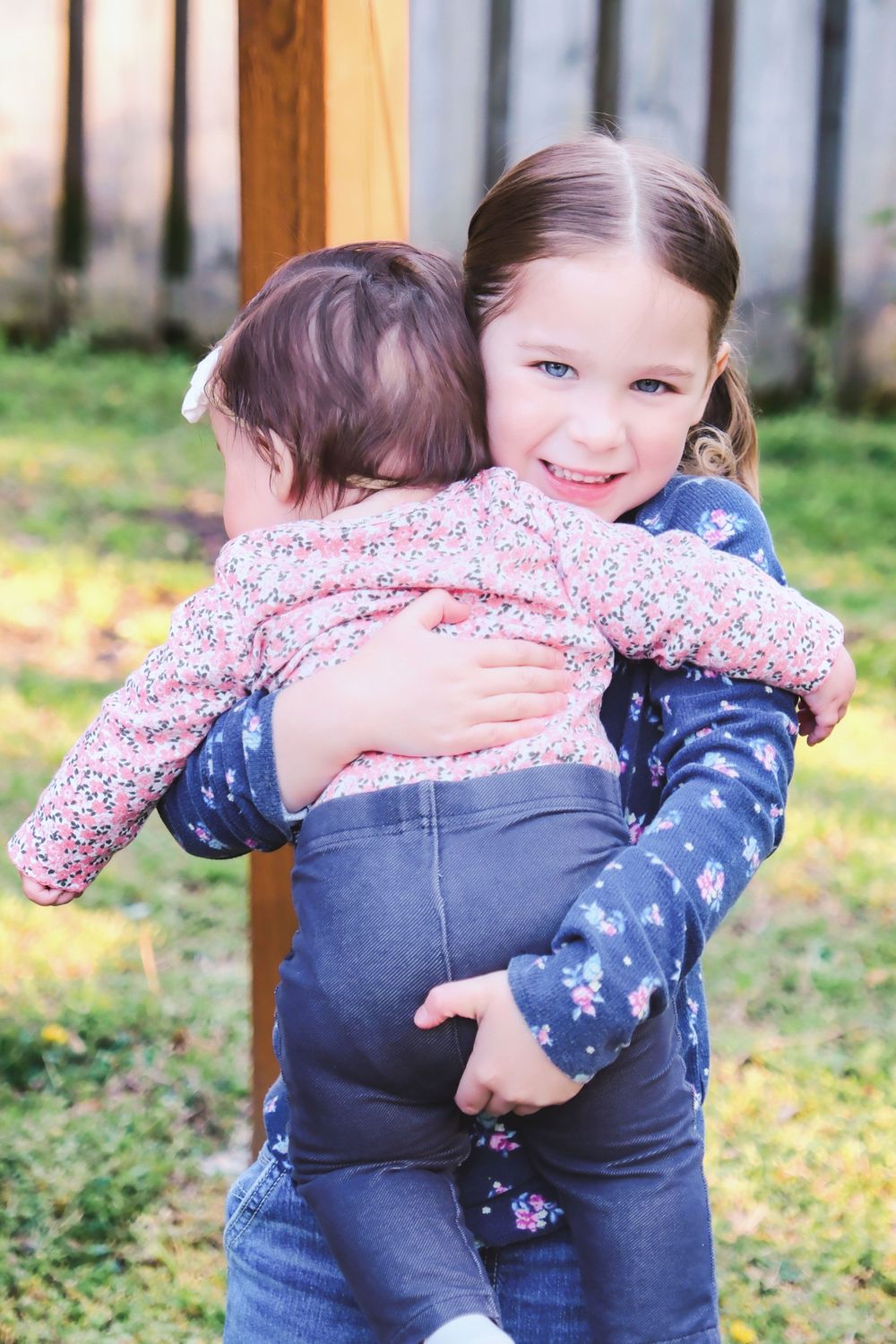 Two children embrace outdoors while wearing matching floral and star print clothing on a sunny day.