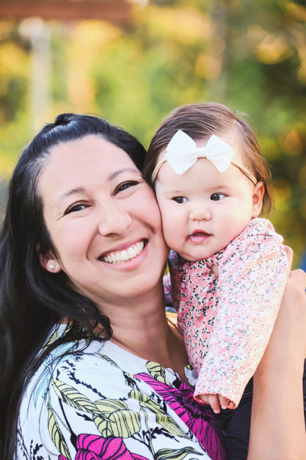 A joyful outdoor portrait shows a mother and baby in front of a softly blurred natural backdrop.