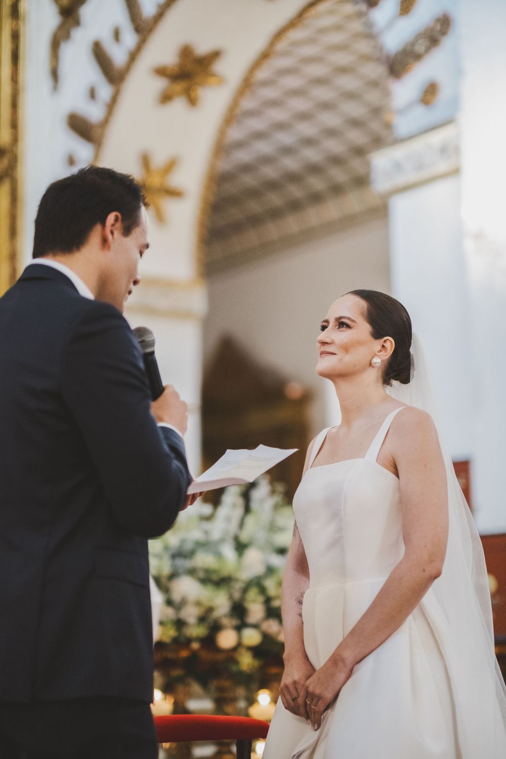 A wedding ceremony in progress showing a couple exchanging vows beneath an ornate arched ceiling with gold stars.