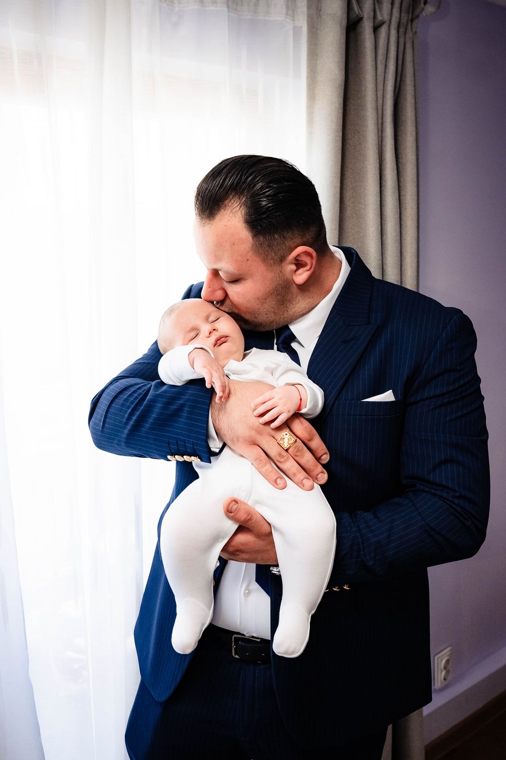 Person in navy suit tenderly kissing a baby dressed in white.