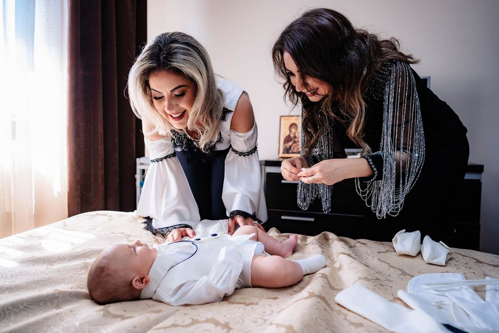 Two women looking down at a baby lying on white bedding.