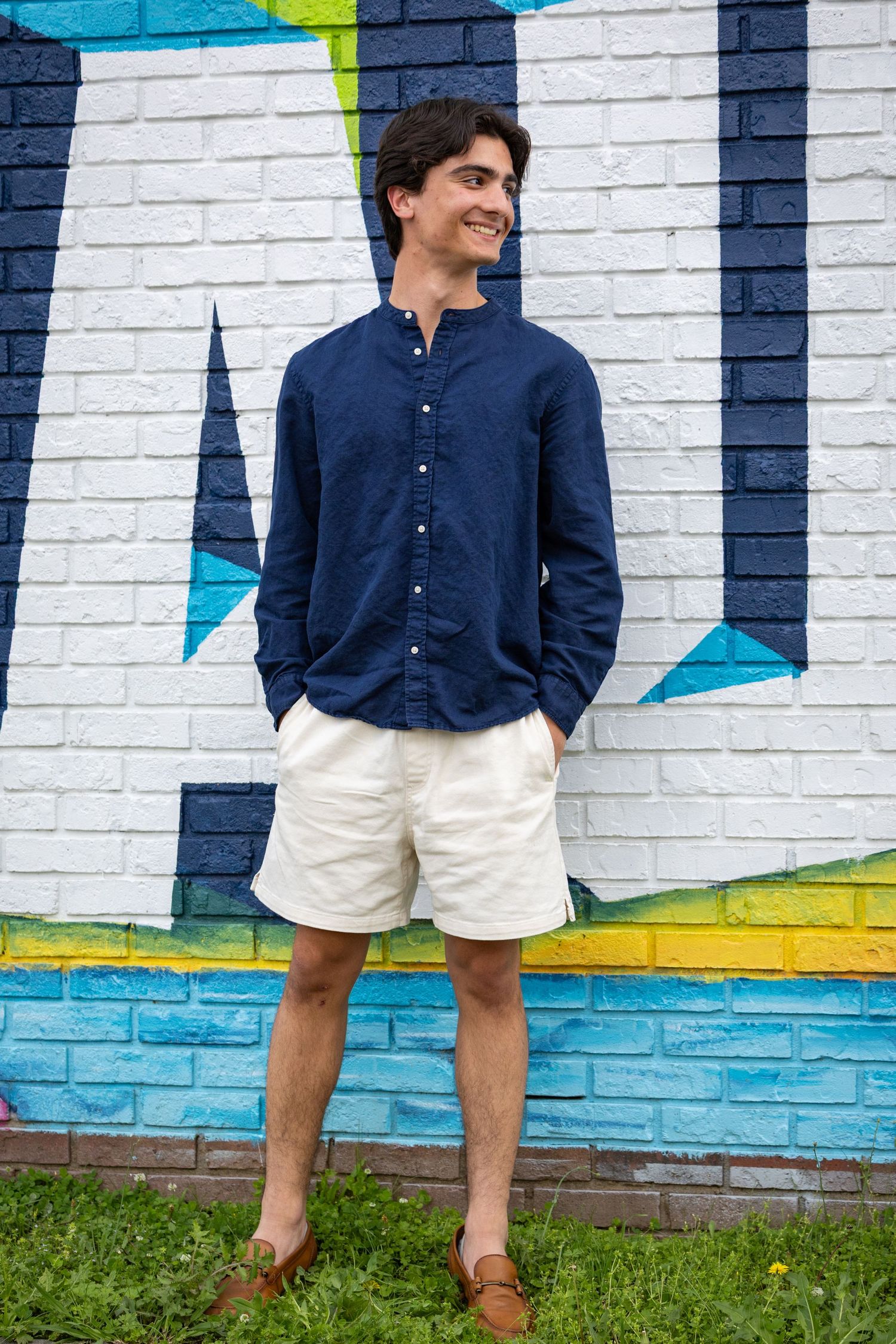 Person in navy shirt and white shorts stands against brick wall with geometric patterns.