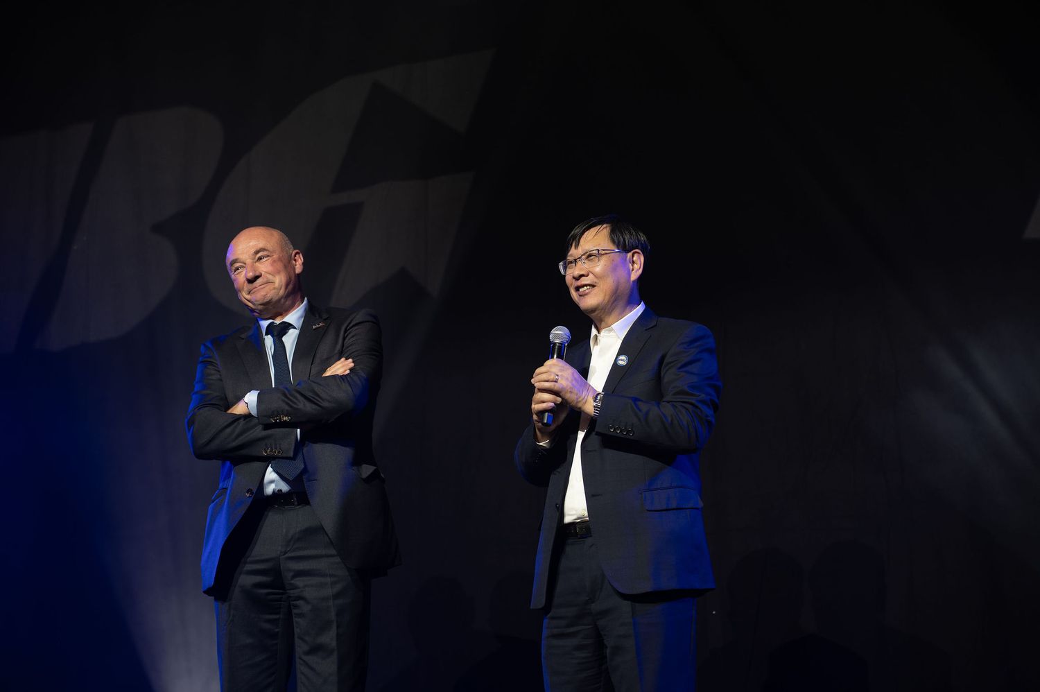 Deux dirigeants d'entreprise sur scène lors d'un événement professionnel, l'un d'eux prend la parole avec un micro.