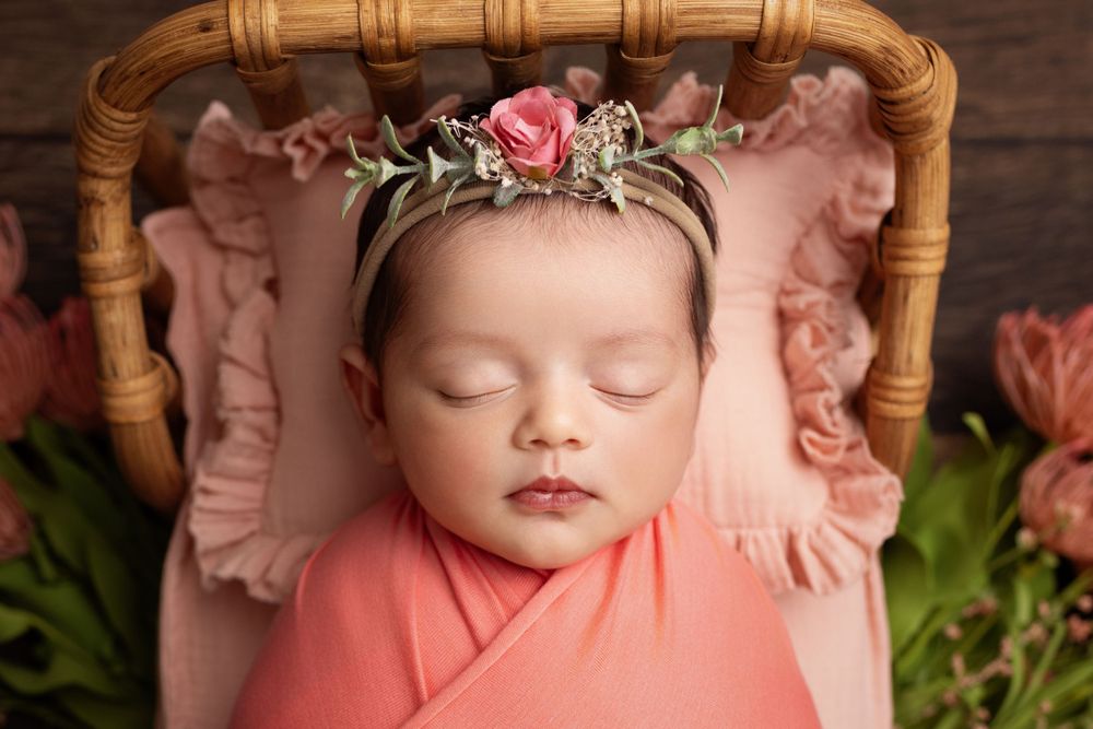 Delicate pink floral crown adorns a peaceful sleeping newborn on a peach pillow.