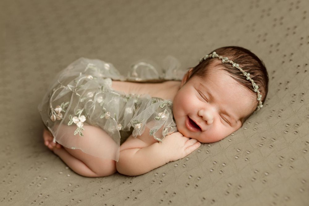 newborn baby girl smiling in  bum up pose, wearing a dainty beaded headband