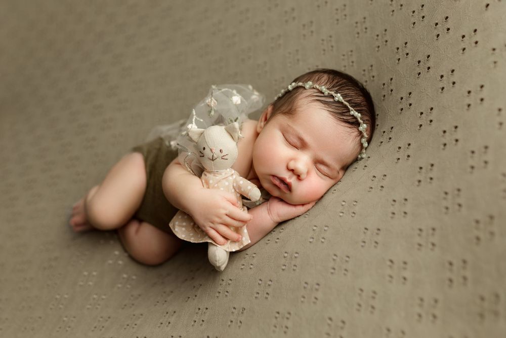 newborn baby girl posing in side laying pose with a lovie