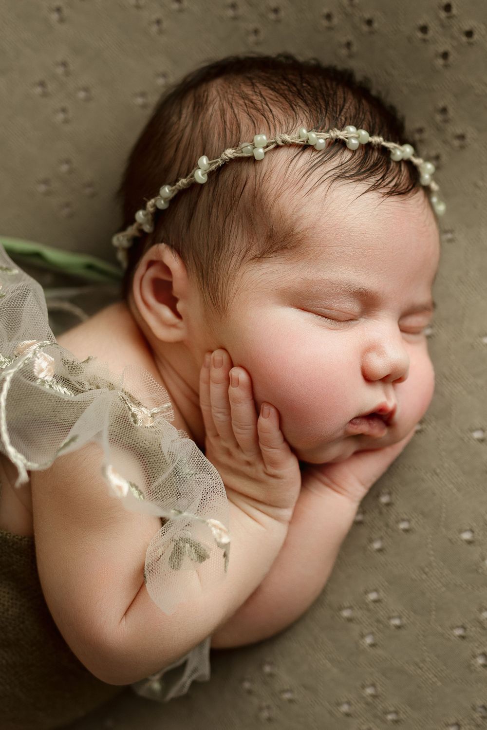 newborn baby girl posing with hands on chubby cheeks, wearing a dainty beaded headband during her newborn photo shoot in cedar park tx