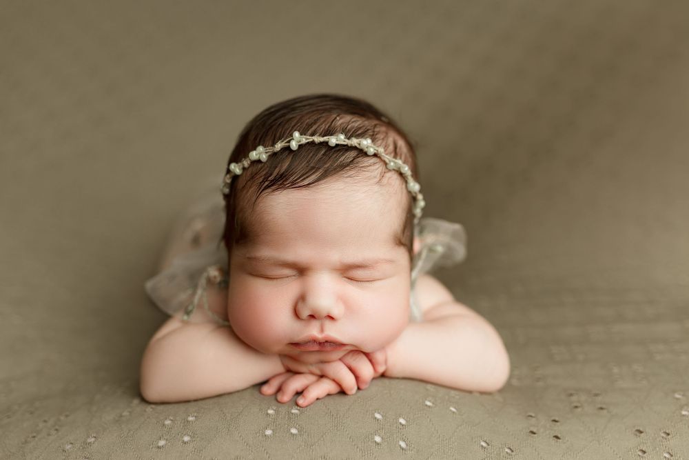 newborn baby girl posing with chin on hands, wearing a dainty beaded headband in austin tx