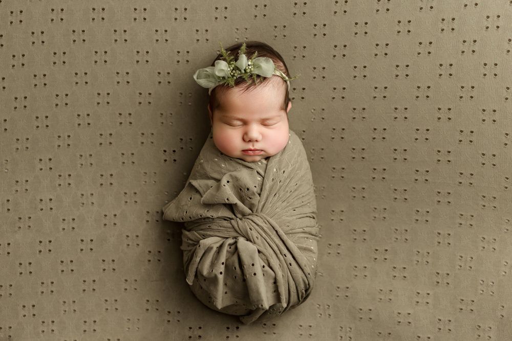 newborn baby girl asleep on back, wrap in green with a bow during newborn photo session in leander tx