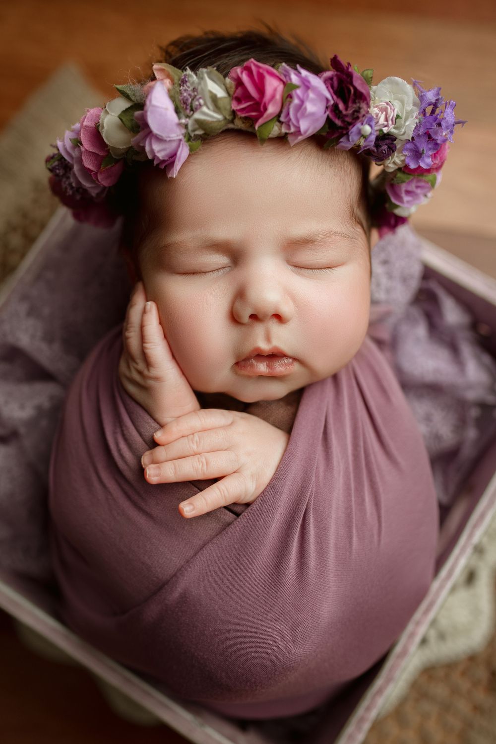 Sleeping newborn wrapped in purple fabric wearing a delicate floral crown of pink and purple roses in cedar park's  premier photo studio