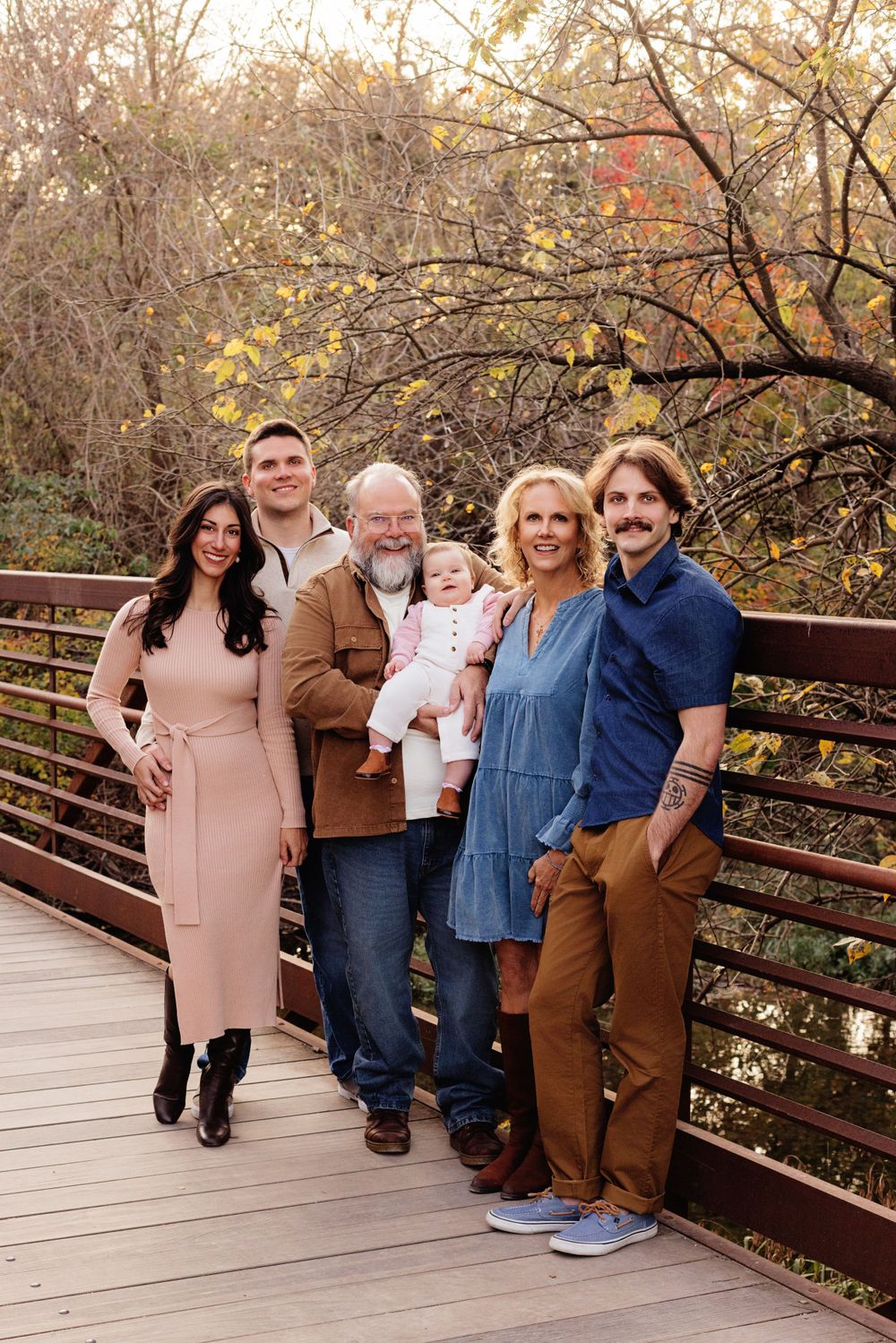 A family stands together on a wooden bridge surrounded by autumn trees during an outdoor photo session.