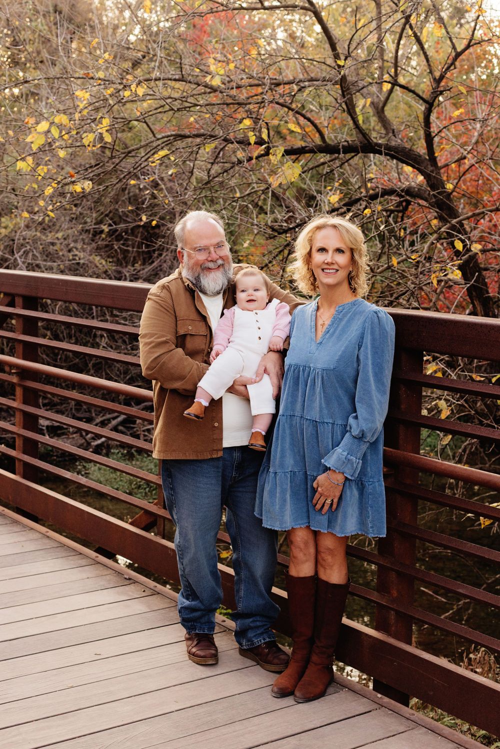A family poses together on a wooden bridge during autumn with fall foliage in the background.