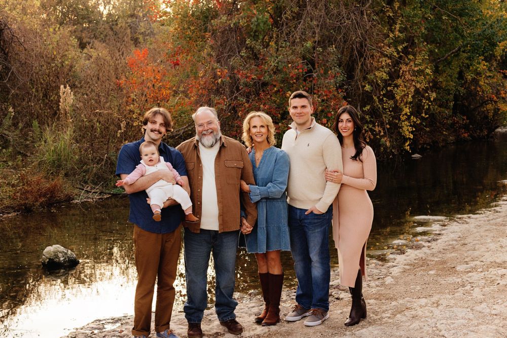 A group of people standing together on an autumn path by a pond in warm fall colors during a family photoshoot.