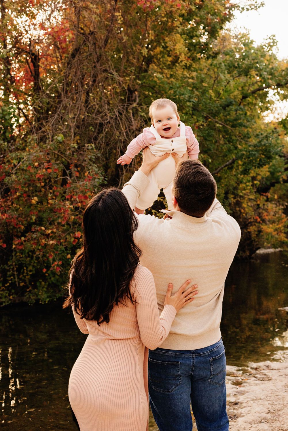 A family enjoys an autumn day together by a lake with fall foliage in the background.