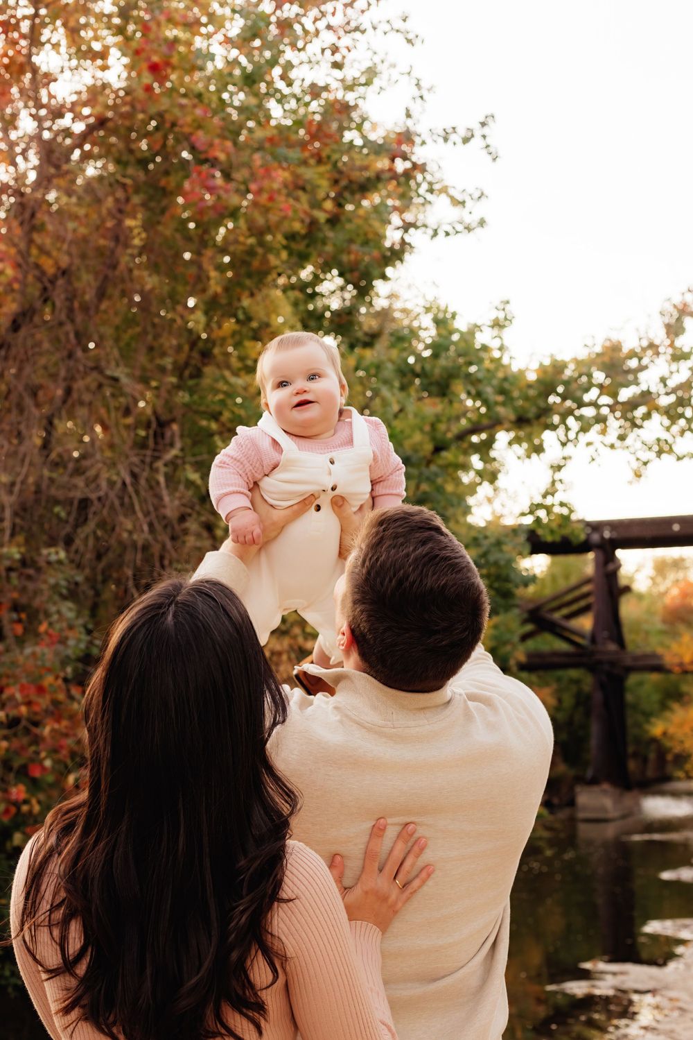 Family shares a joyful autumn moment by the water with colorful fall foliage in the background.