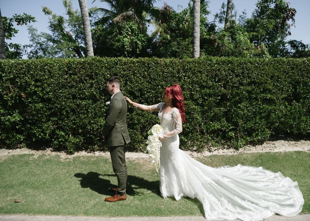 Wedding ceremony outdoors with couple standing against lush green hedge backdrop.