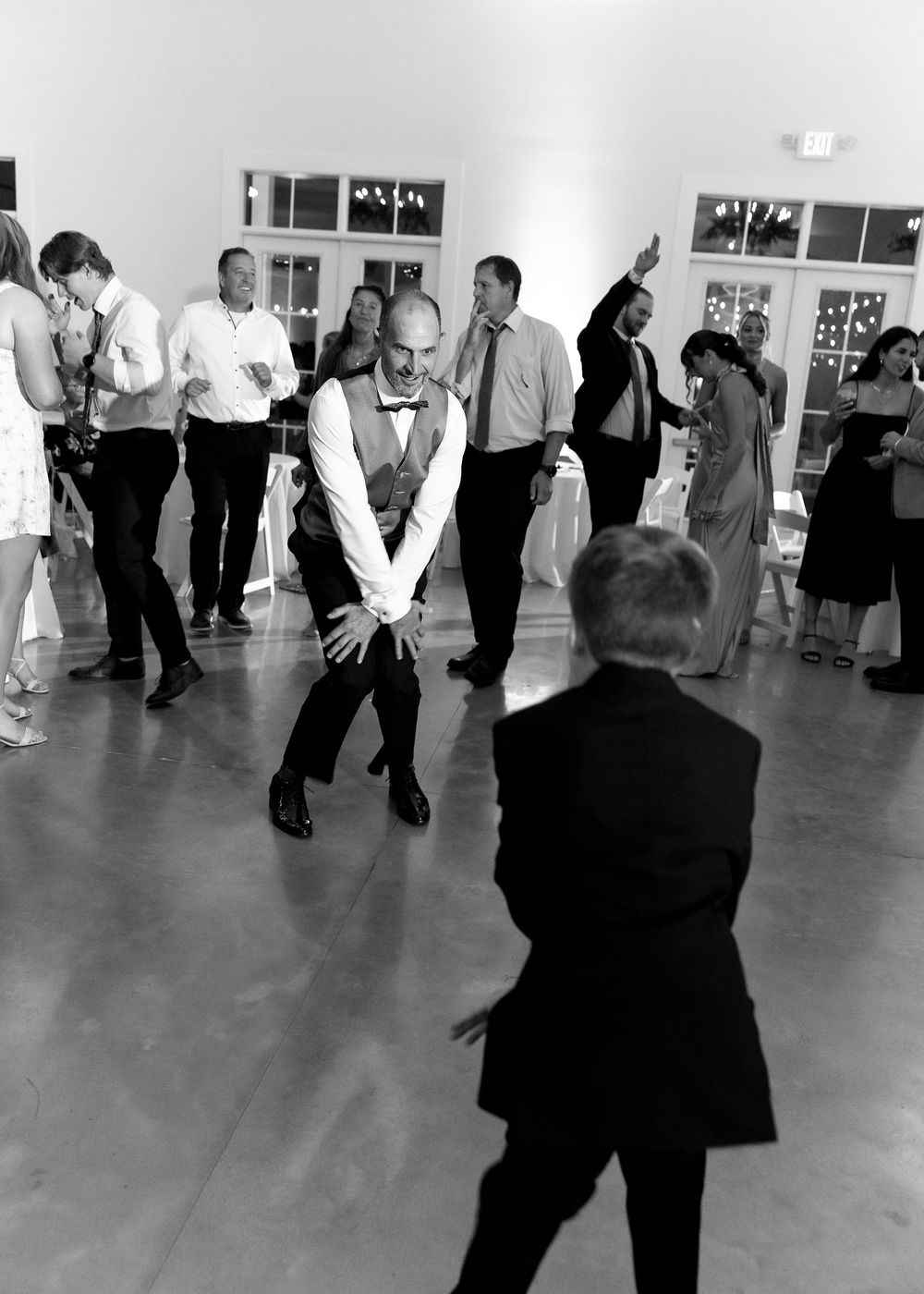 Black and white photo of wedding guests dancing energetically on a reception dance floor.
