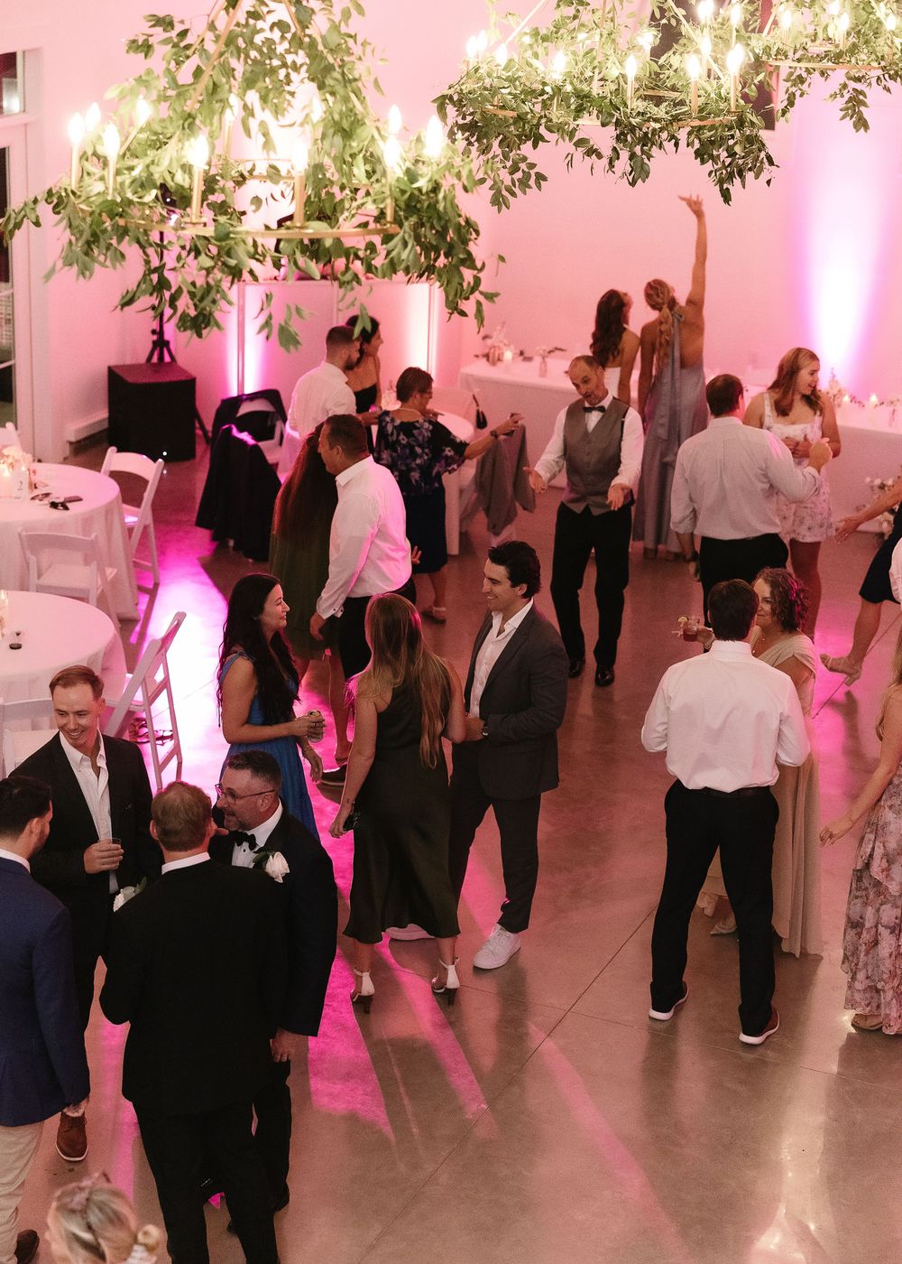 Wedding reception guests dancing on a dance floor illuminated with pink lighting in an elegant venue.