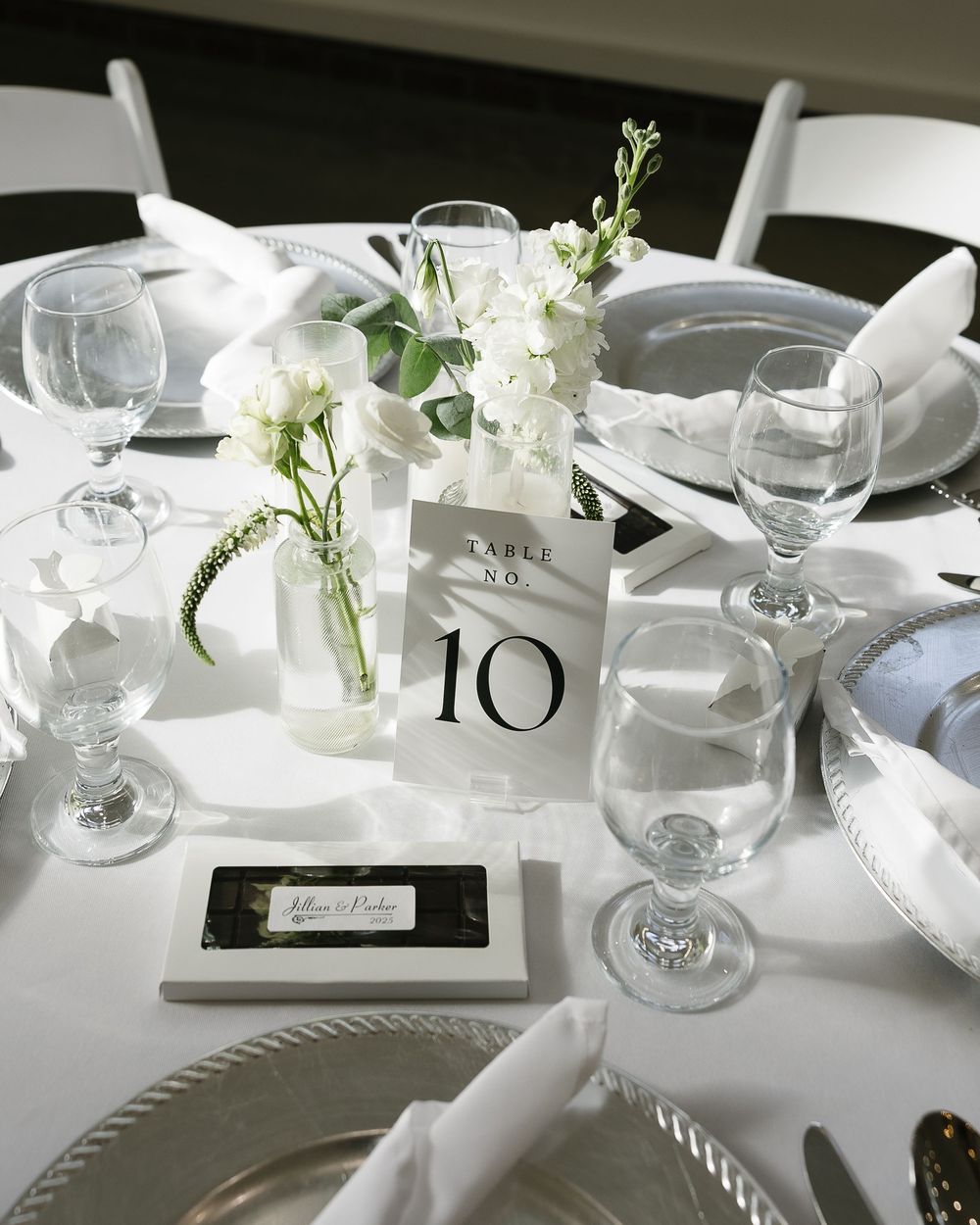 Minimalist wedding table decor with white flowers, table numbers, and place settings.