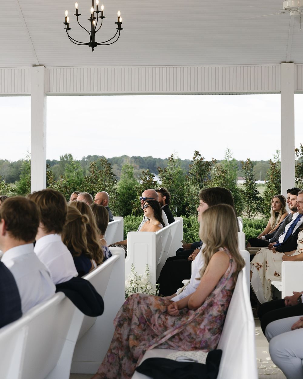Wedding ceremony guests seated under a white covered porch with chandelier overhead.