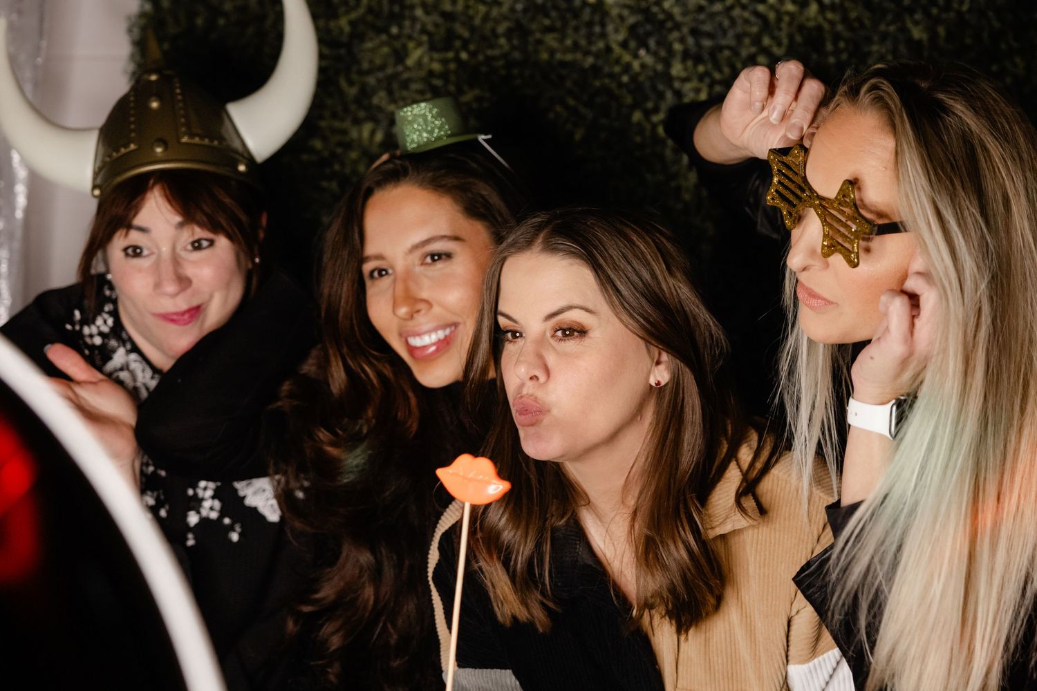 A group of friends pose together at a party wearing festive holiday accessories and making playful expressions.