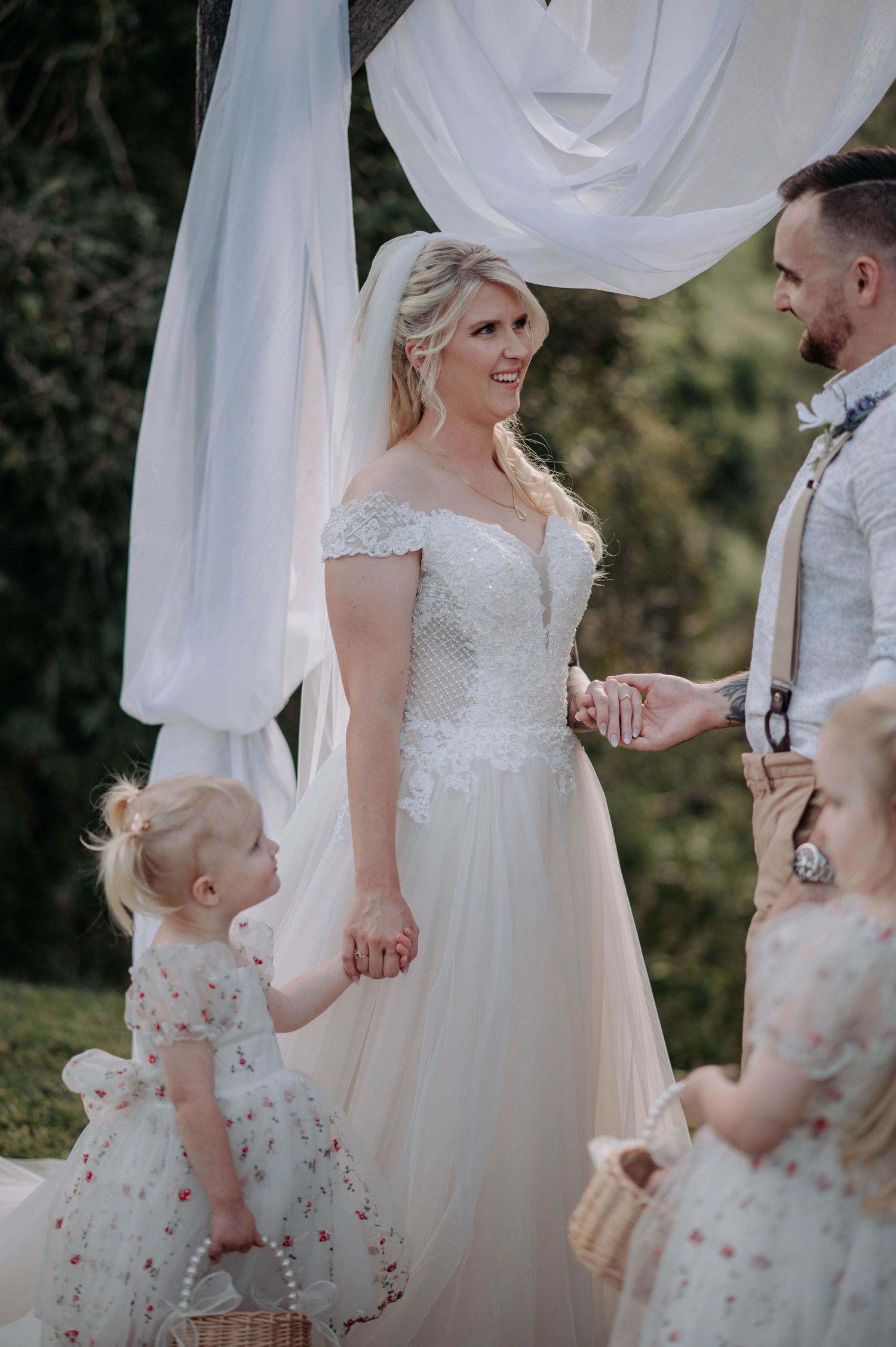 Outdoor wedding ceremony with couple standing under white draped arch.