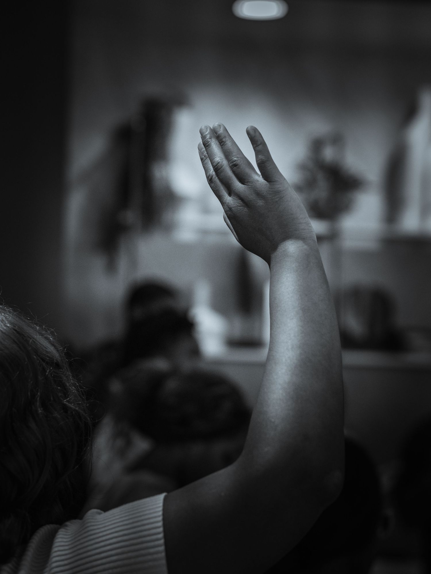 A person in casual attire with hands clasped over heart during worship.