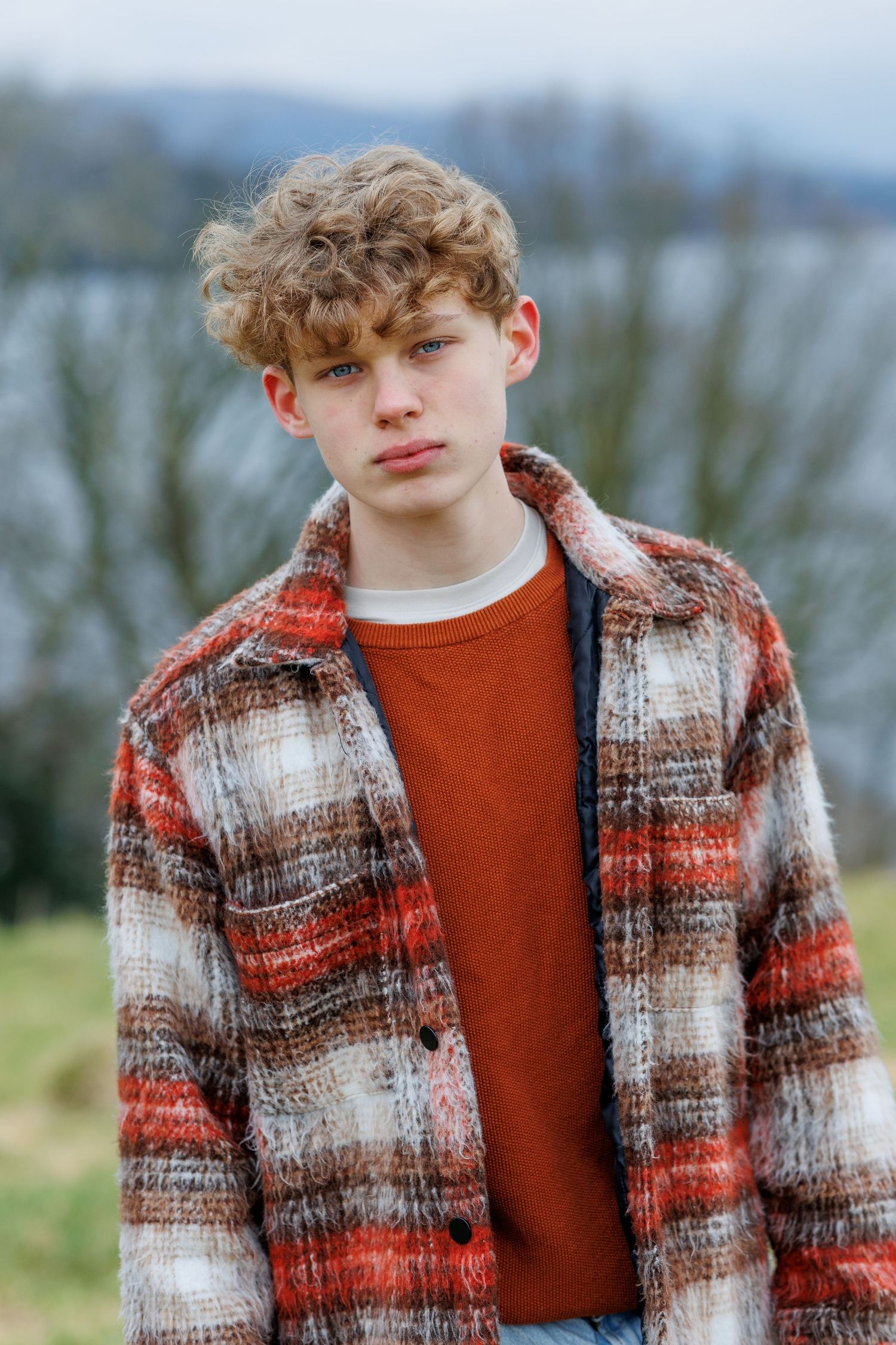 Person wearing a cozy plaid winter coat in red and white tones against a blurred outdoor background.