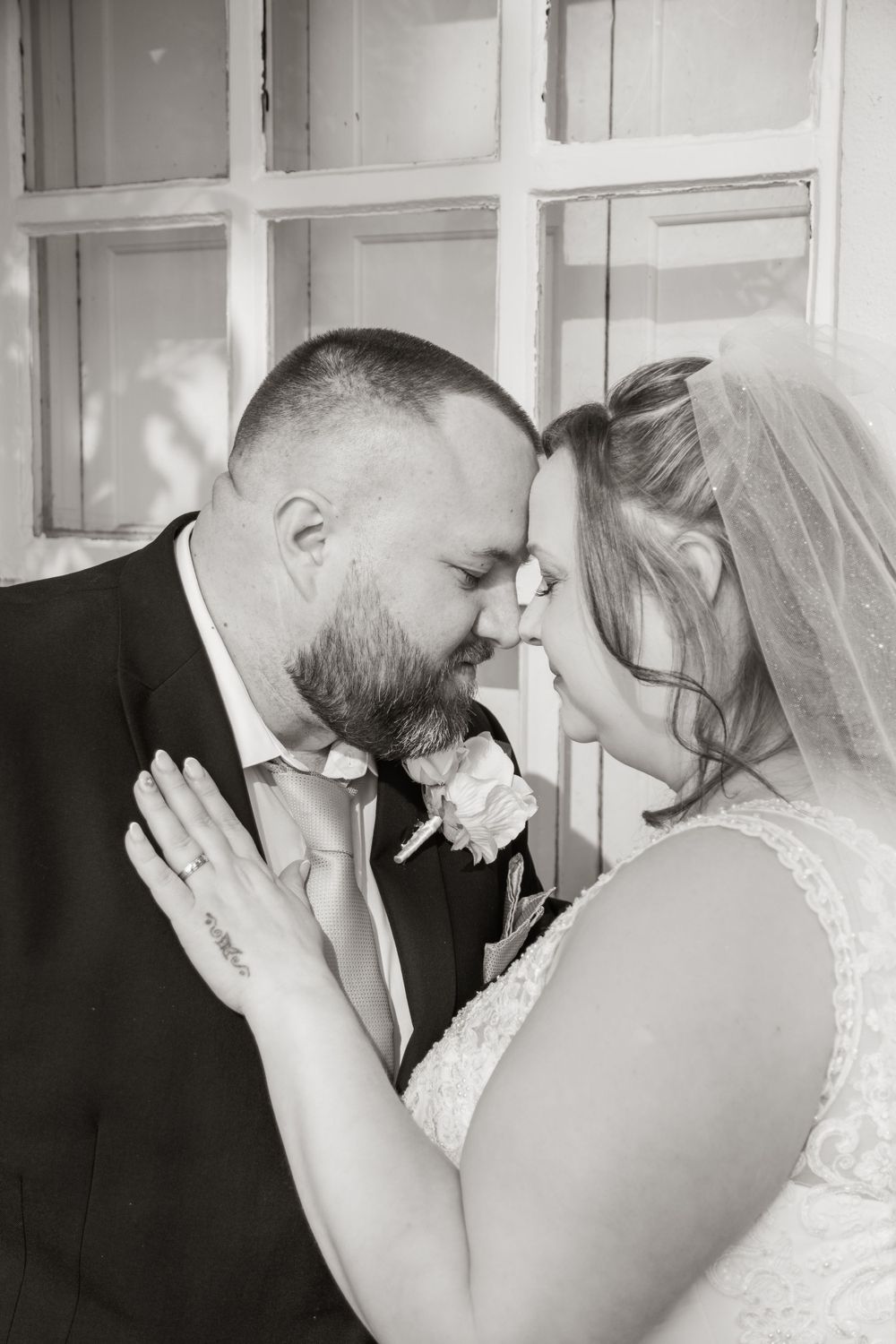 A tender black and white wedding moment of a romantic couple sharing an intimate moment by a window.