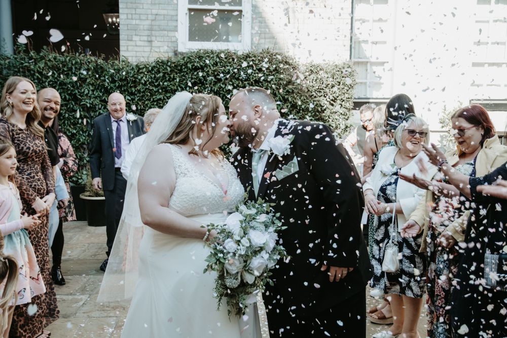 Wedding couple shares a joyful moment as guests shower them with confetti outside a brick building.