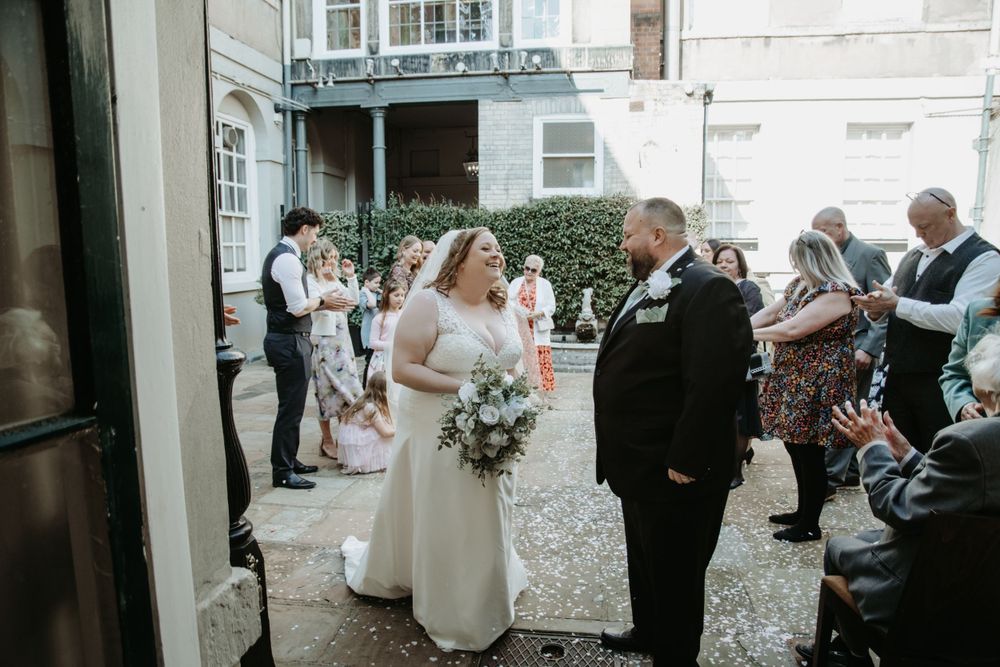 A bride and groom share a joyful moment outside a historic building during their intimate wedding ceremony.