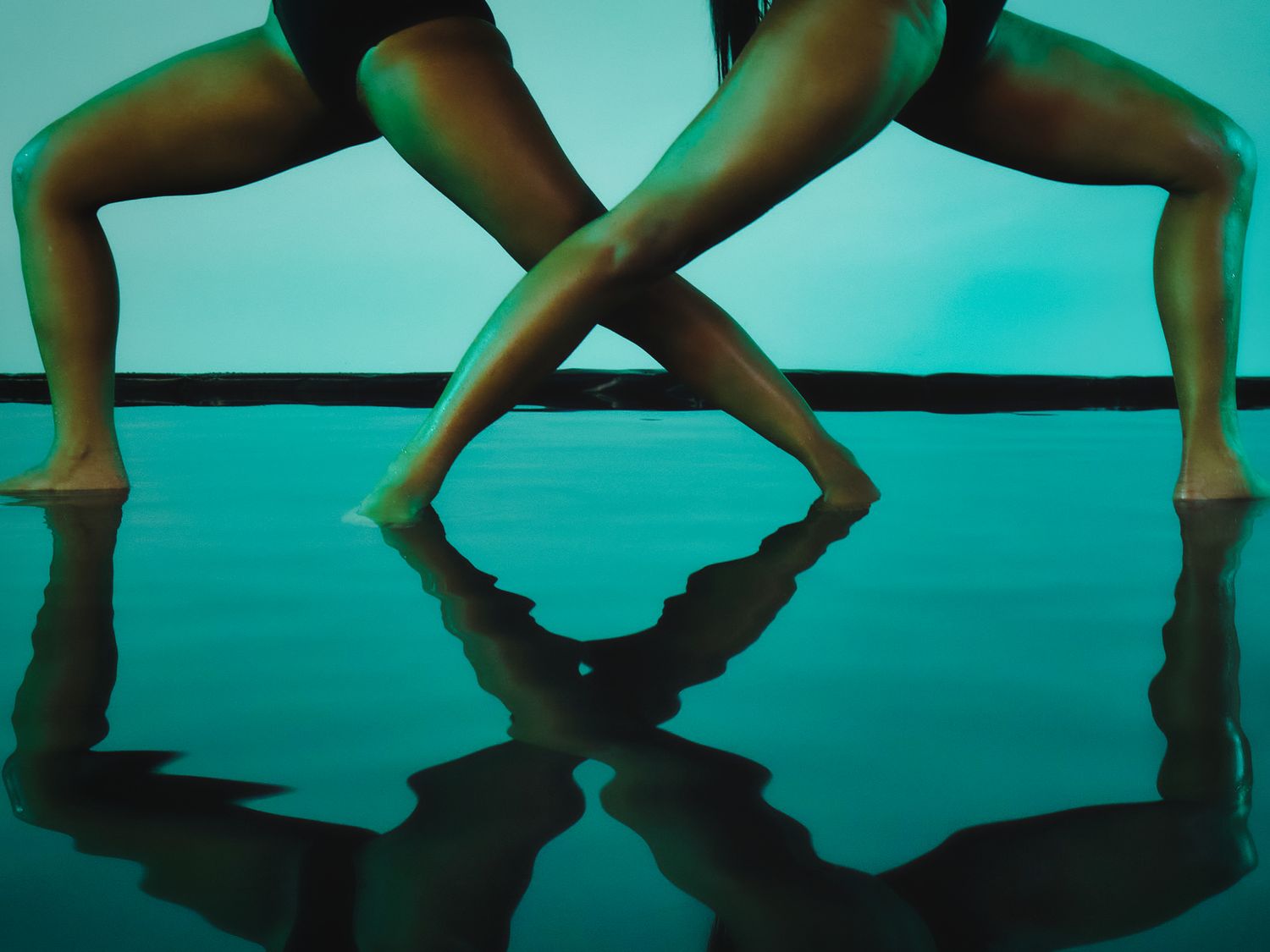 Artistic dance photo showing crossed legs reflected in turquoise water.