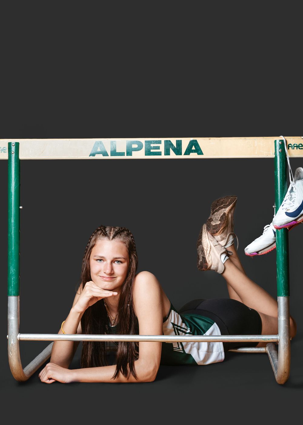 Young female track athlete posing with an Alpena hurdle, lying down smiling in athletic wear.