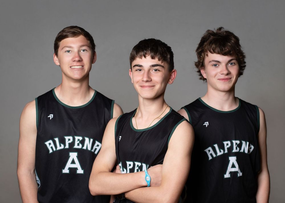 Three young male athletes in black Alpena basketball jerseys pose together for a team portrait photo.