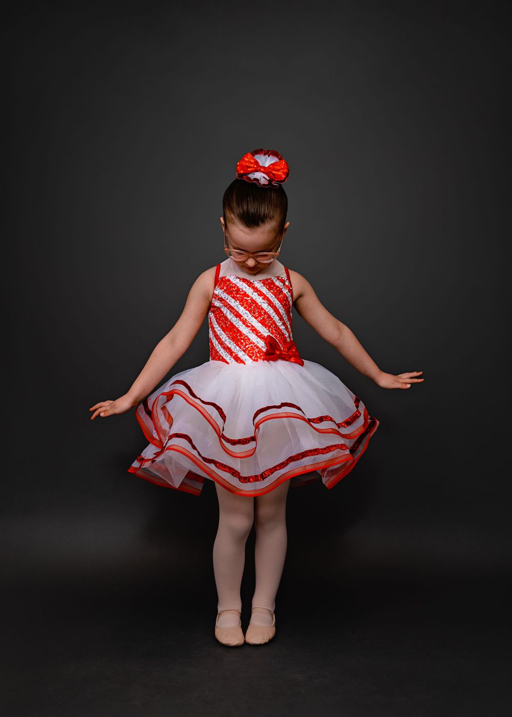 A dancer in a festive red and white candy cane striped dress with tulle skirt twirls against a dark background.