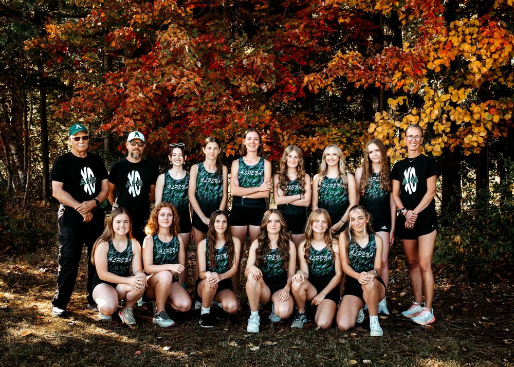 High school cross country team poses together in matching uniforms against vibrant autumn foliage backdrop.