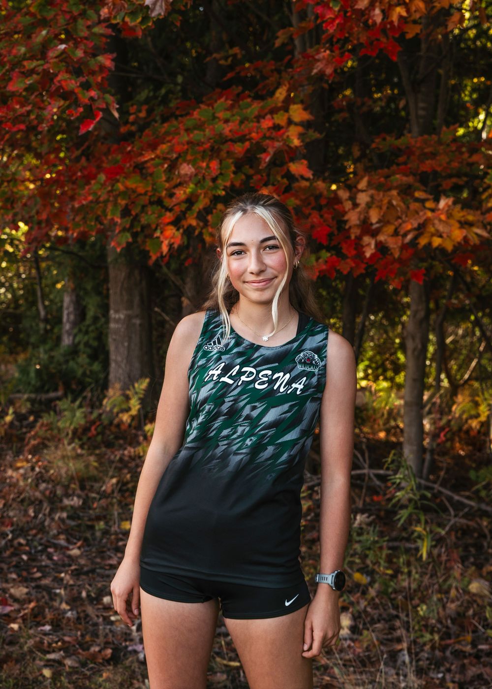 Athlete in dark athletic wear poses against vibrant autumn foliage with red and orange leaves in the background.