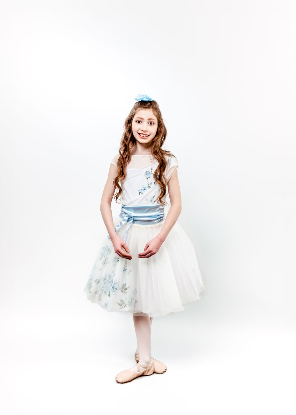 A young dancer in a light blue and white tulle dress with floral details poses gracefully against a white background.