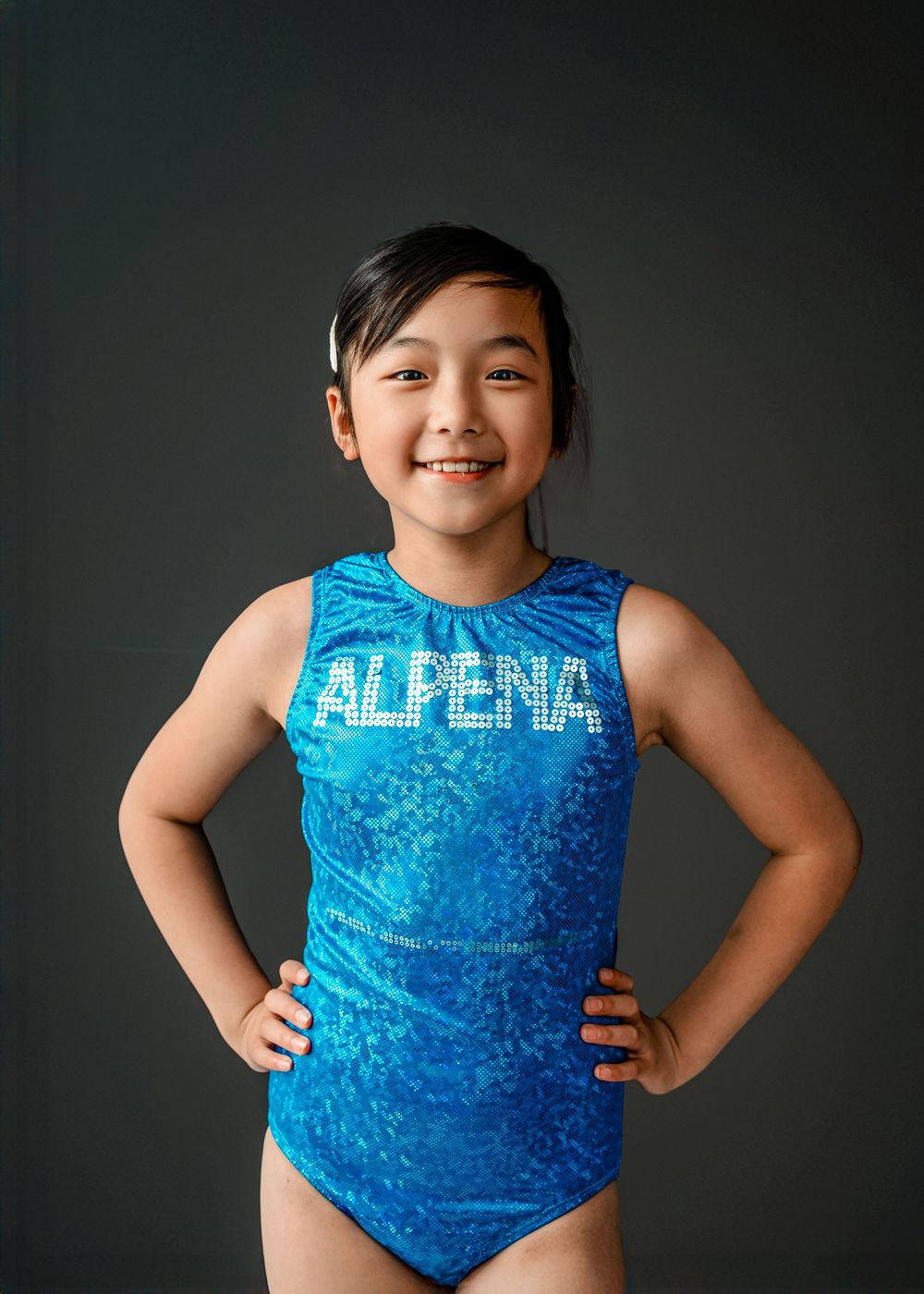 A young gymnast in a bright blue velvet leotard poses confidently against a dark background in a series of photos.