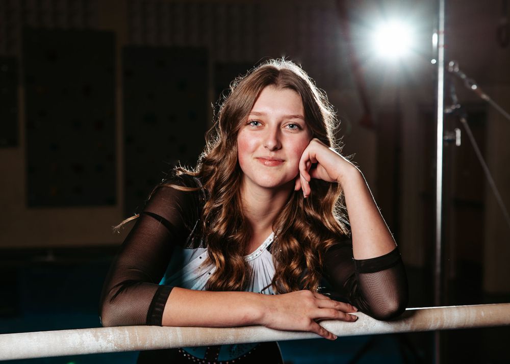 Portrait of a person with long wavy hair in a black mesh top leaning on a countertop with dramatic lighting.
