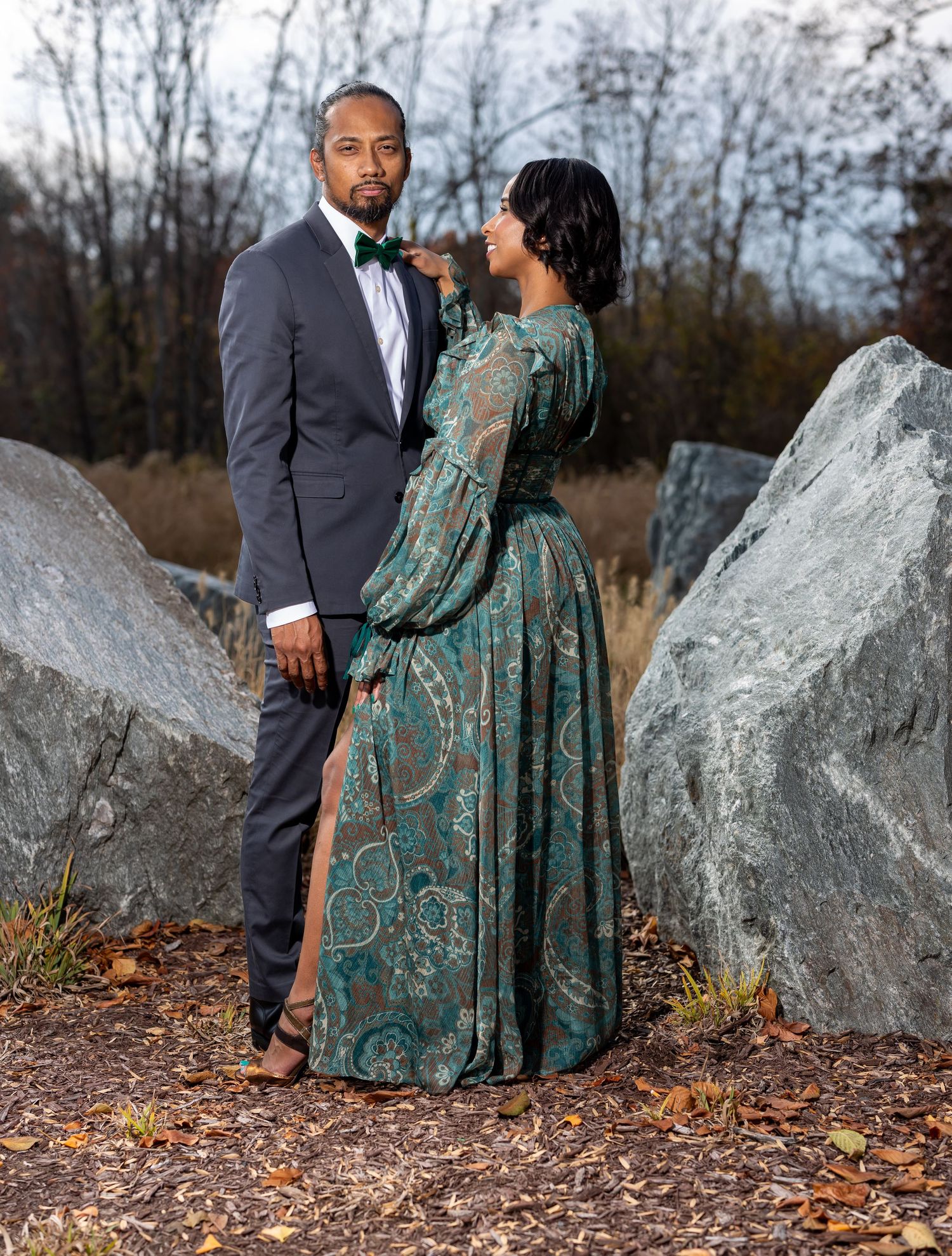 Formal portrait session with a teal gown and charcoal suit among large outdoor rock formations.