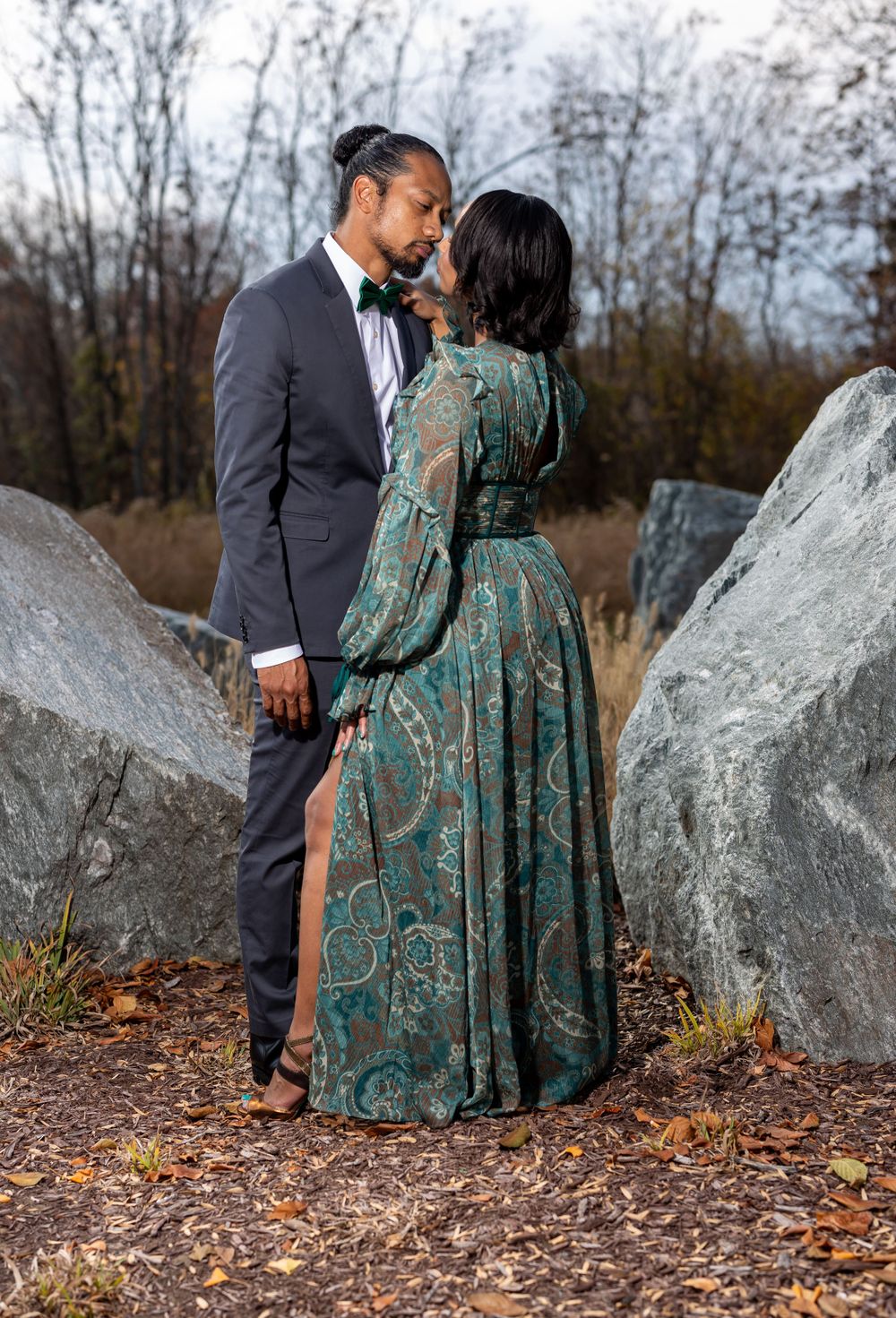 Intimate portrait between large rocks showing a teal dress and dark suit in an autumn setting.