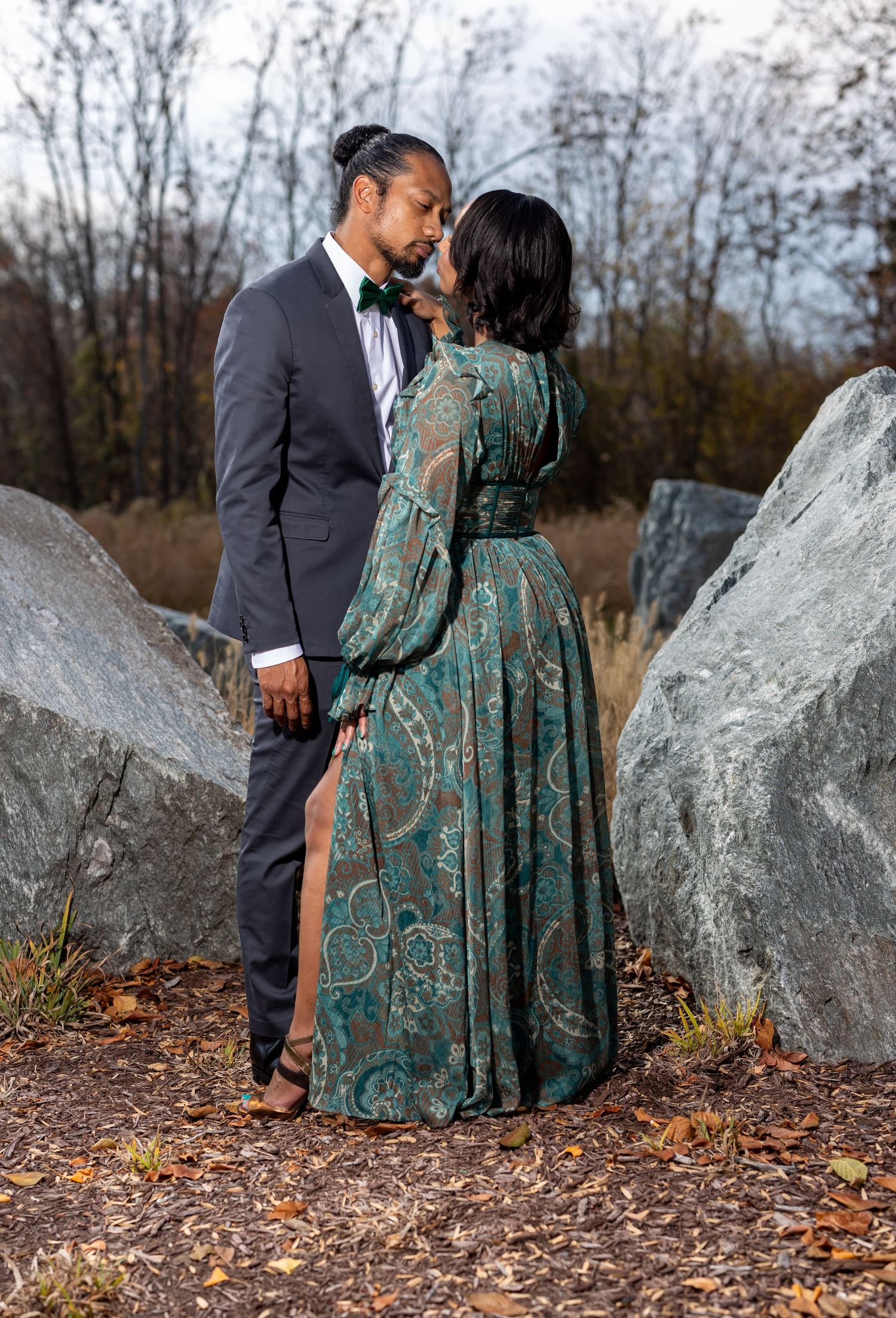 Intimate portrait between large rocks showing a teal dress and dark suit in an autumn setting.