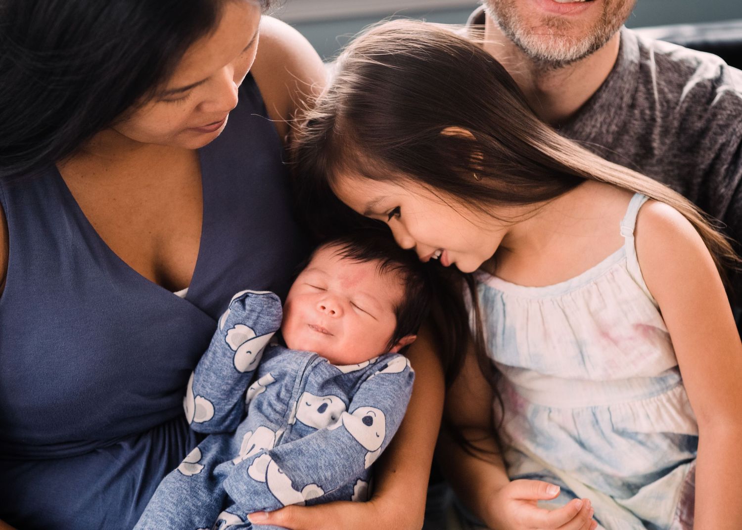 A sweet moment of connection as family members gaze lovingly at a sleeping infant in a blue onesie.