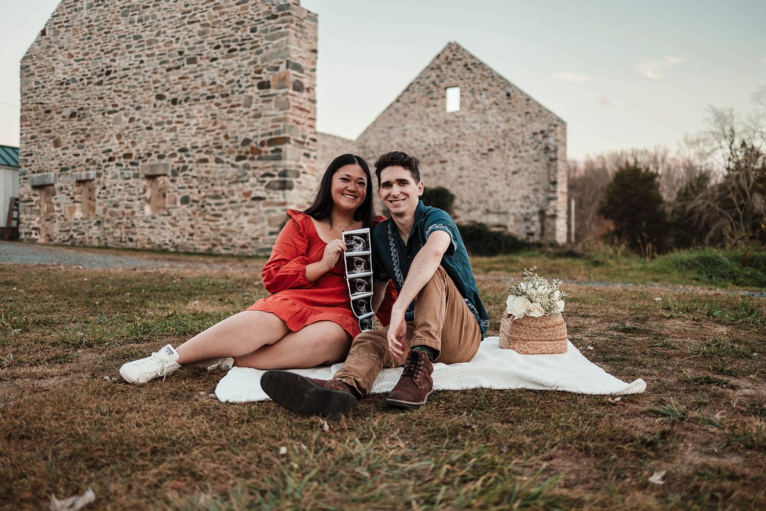 Happy couple expressing joy as they sit outdoors in an open field holding an ultrasound picture, excited to announce their new baby. York PA